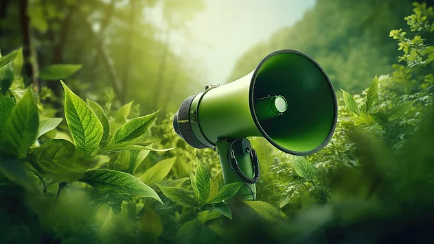 Grünes Megafon steht mitten in dichtem Blattwerk im Wald, umgeben von frischem Grün und weichem Licht.